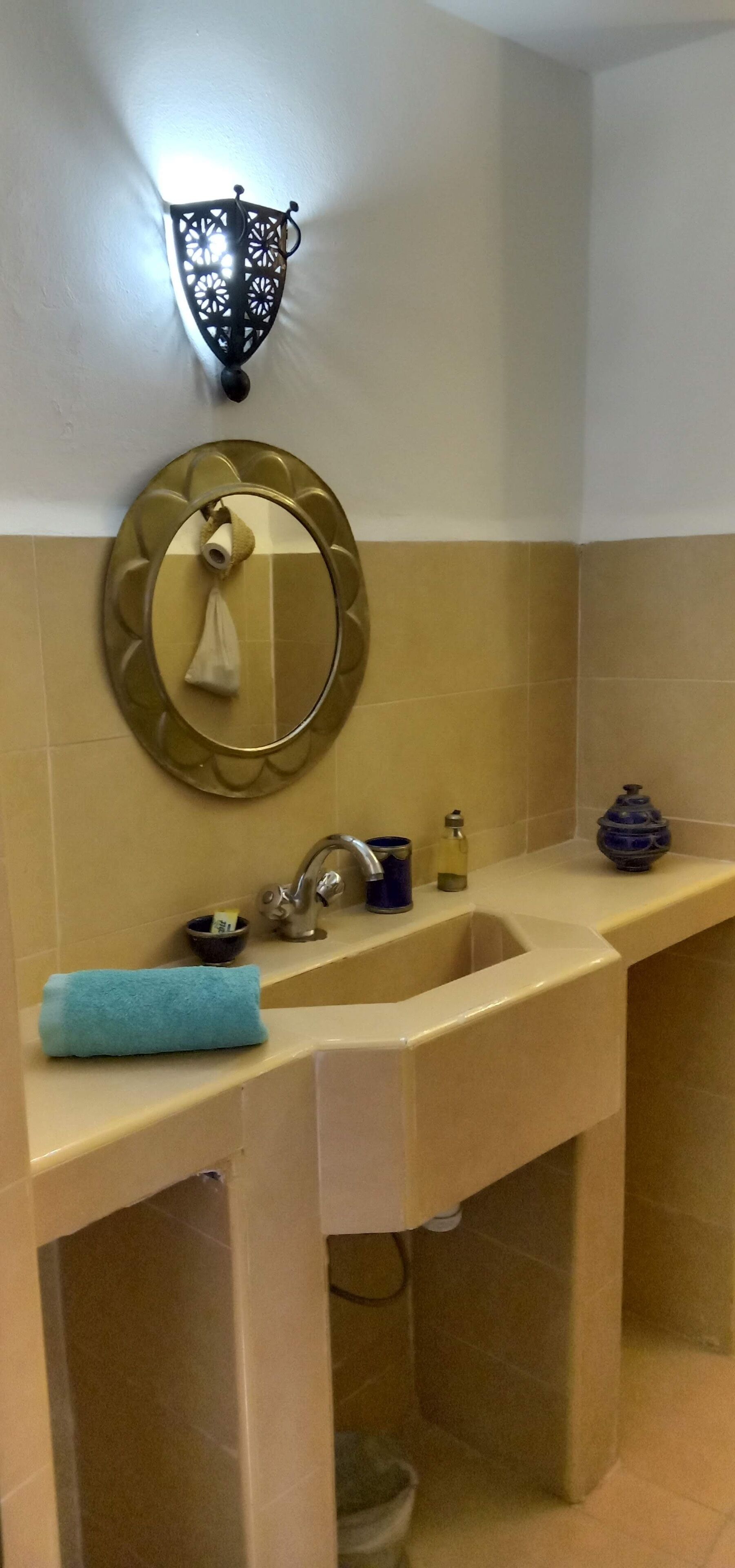 A bathroom with a sink, mirror, towel, soap dispenser, and a decorative wall light.