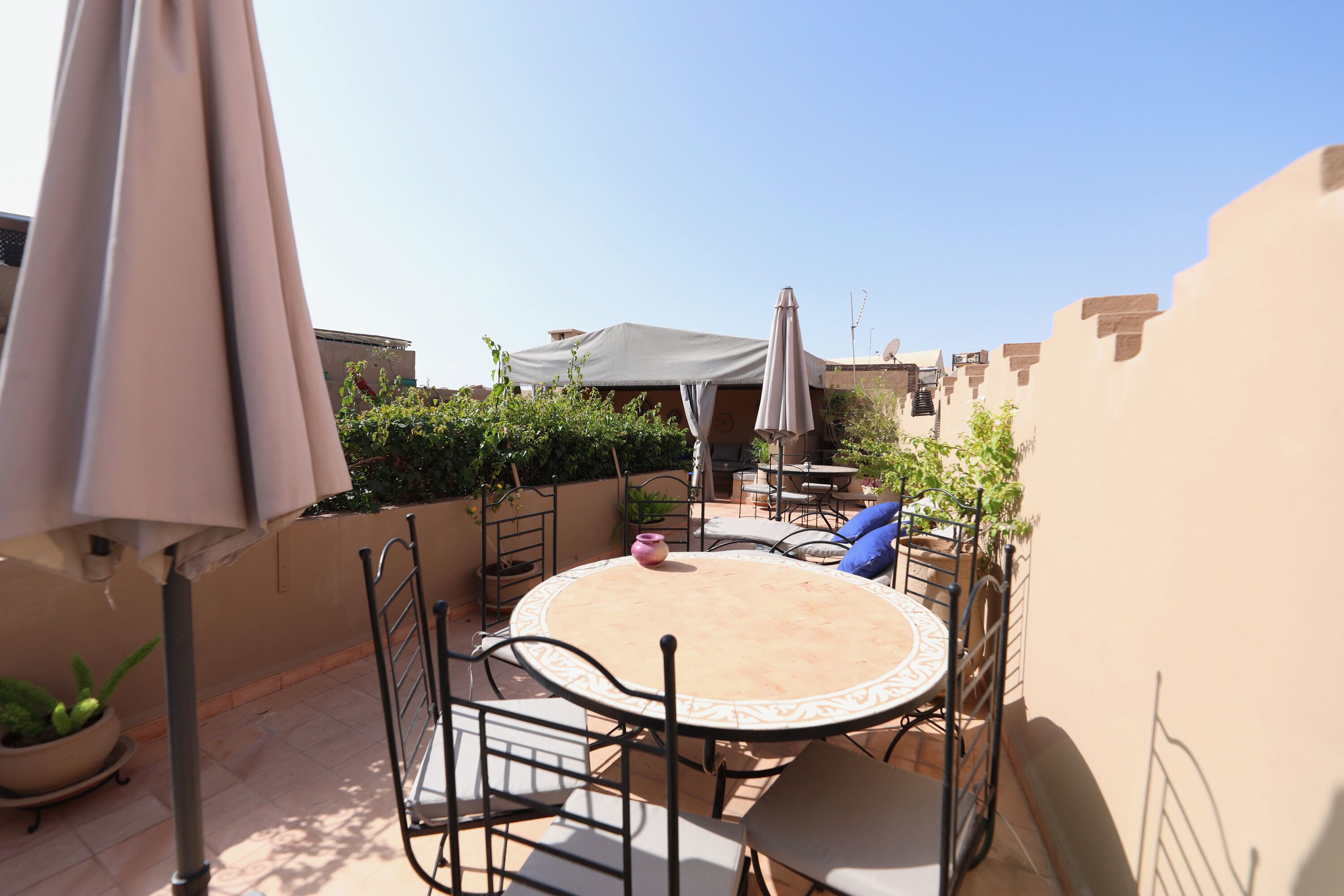 Une terrasse avec une table ronde et des chaises, entourée de plantes en pot et de parasols.