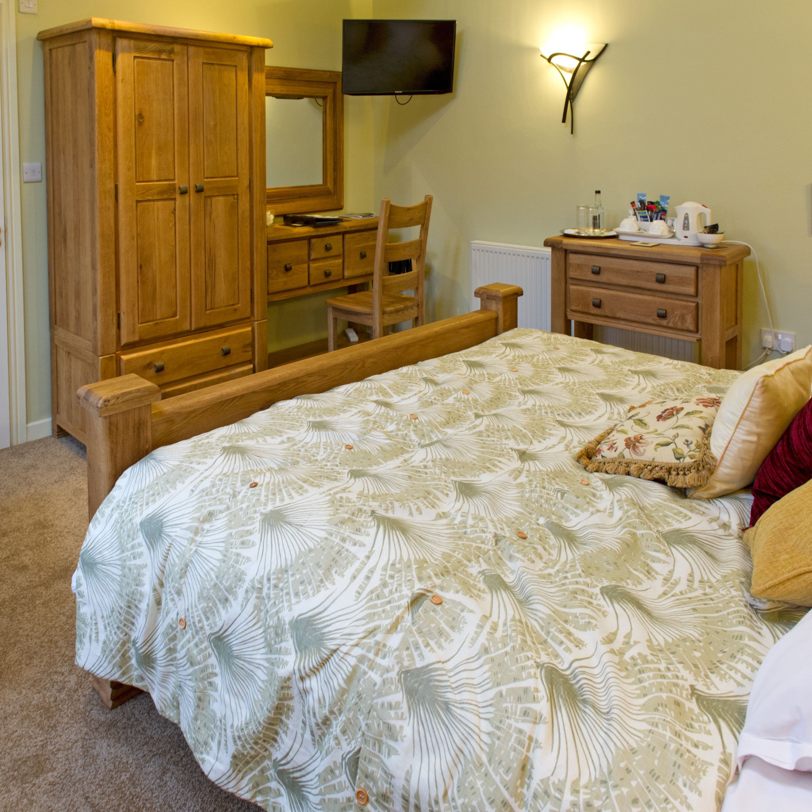 A bedroom with a bed, wooden wardrobe, desk, chair, and a television on the wall.