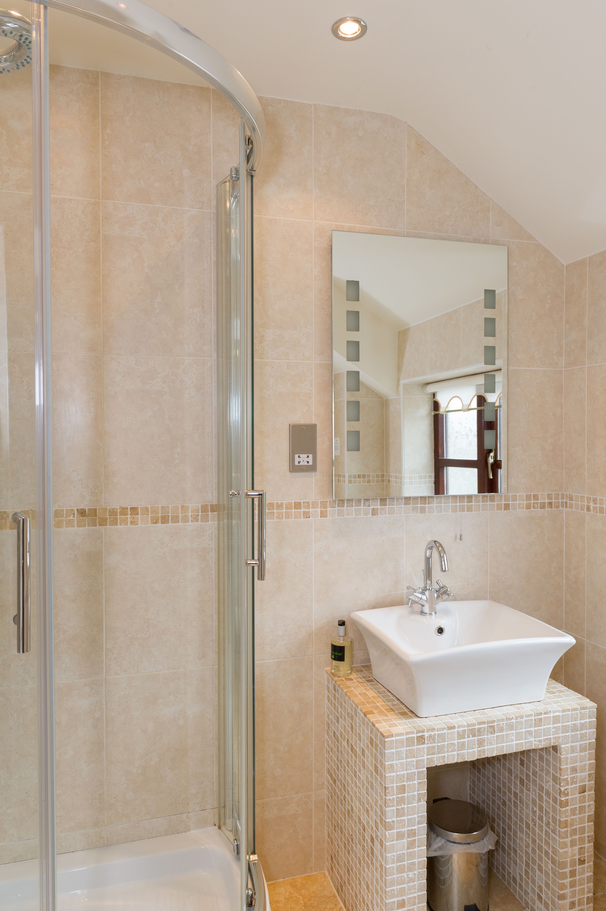 A bathroom with a glass shower enclosure, a sink with a mirror above it, and a tiled floor.