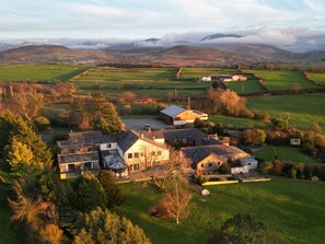 A large estate with multiple buildings, expansive green fields, and a mountainous backdrop. - Ty'n Rhos Country House (Caernarfon)