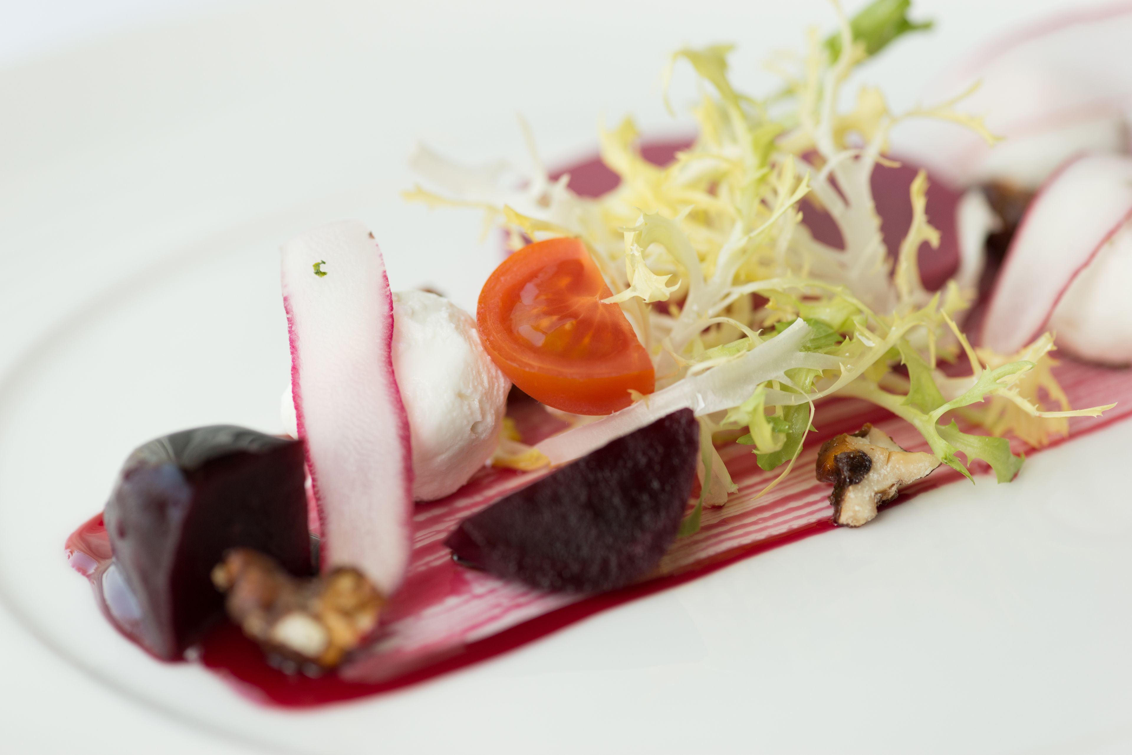 A plate with sliced radishes, a tomato, and some greens.