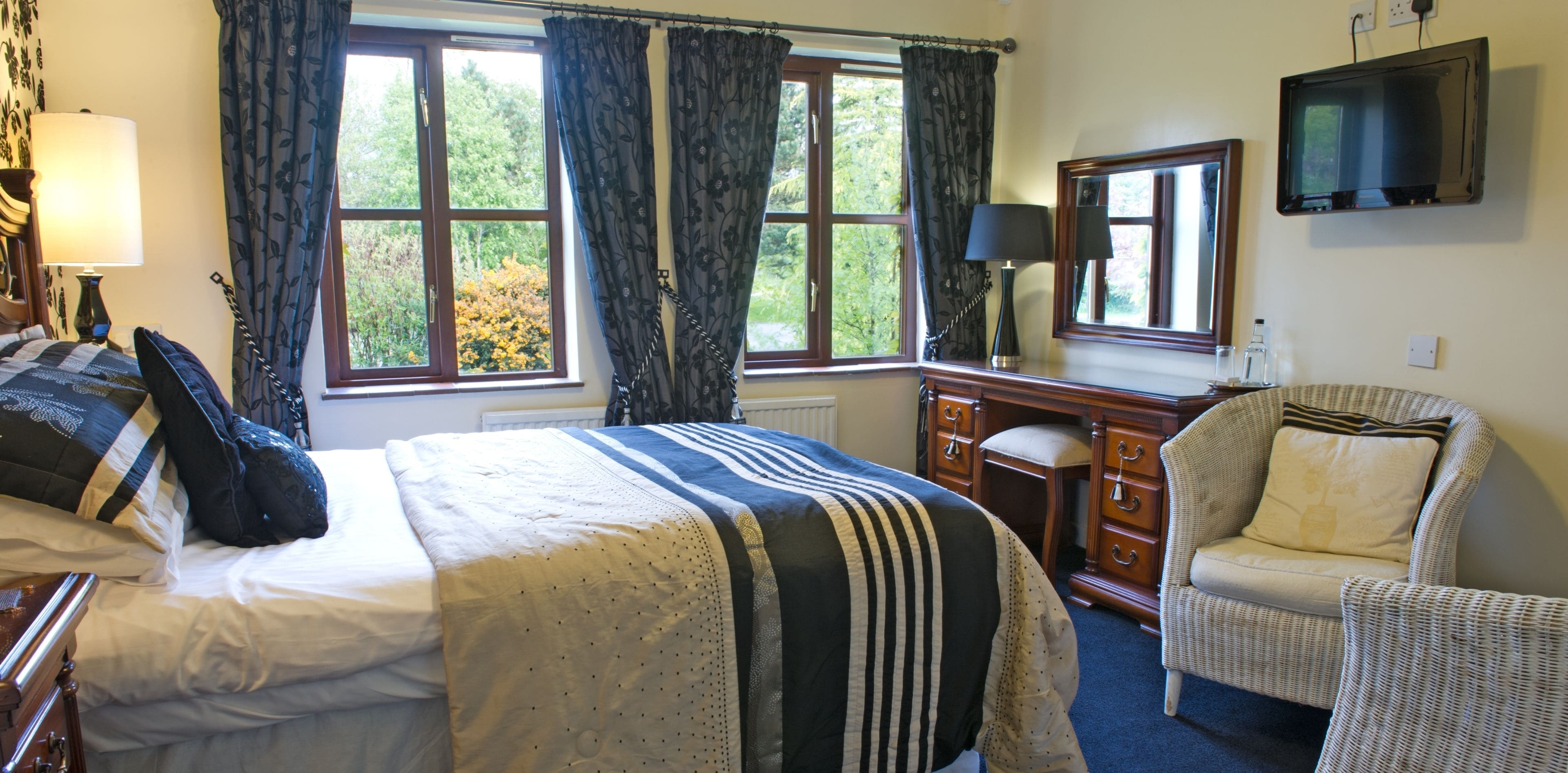 A bedroom with a bed, a dresser, a chair, a television, and a window with curtains.