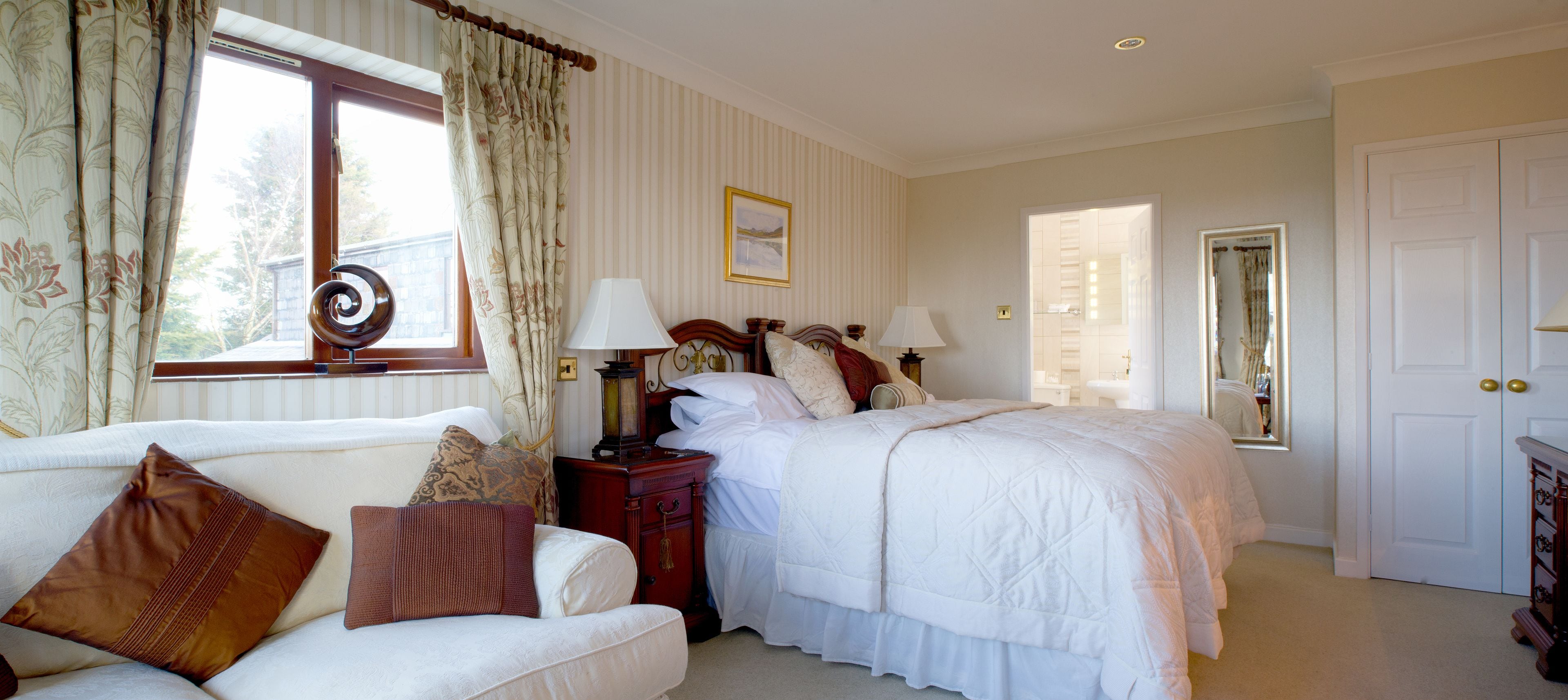 Quarto com cama, mesas de cabeceira, cómoda e janela com cortinas.