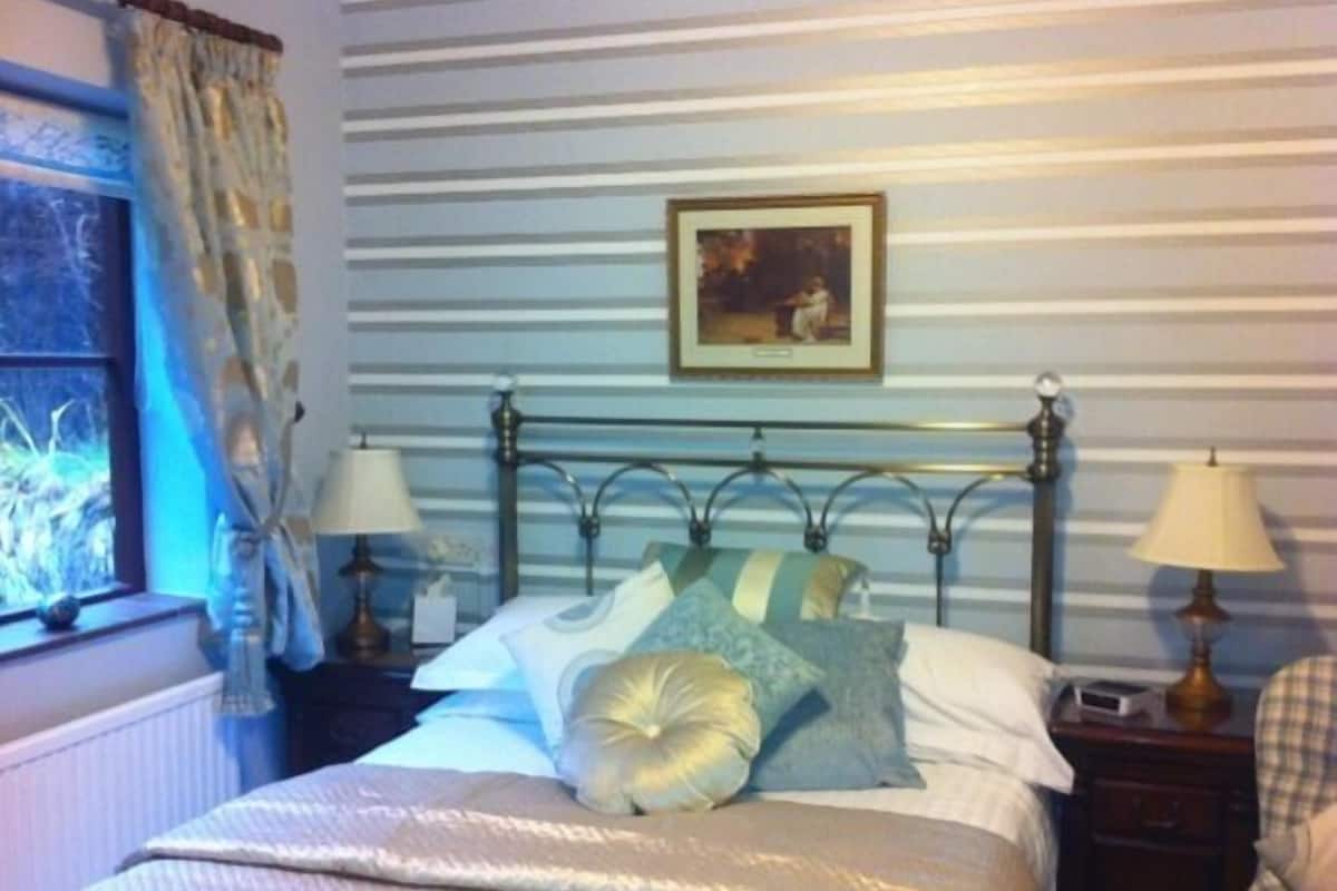 A neatly made bed with a striped wall and a framed picture above it.