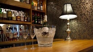 Un coin bar avec une bouteille de champagne dans un récipient en verre, une lampe et diverses bouteilles en arrière-plan.