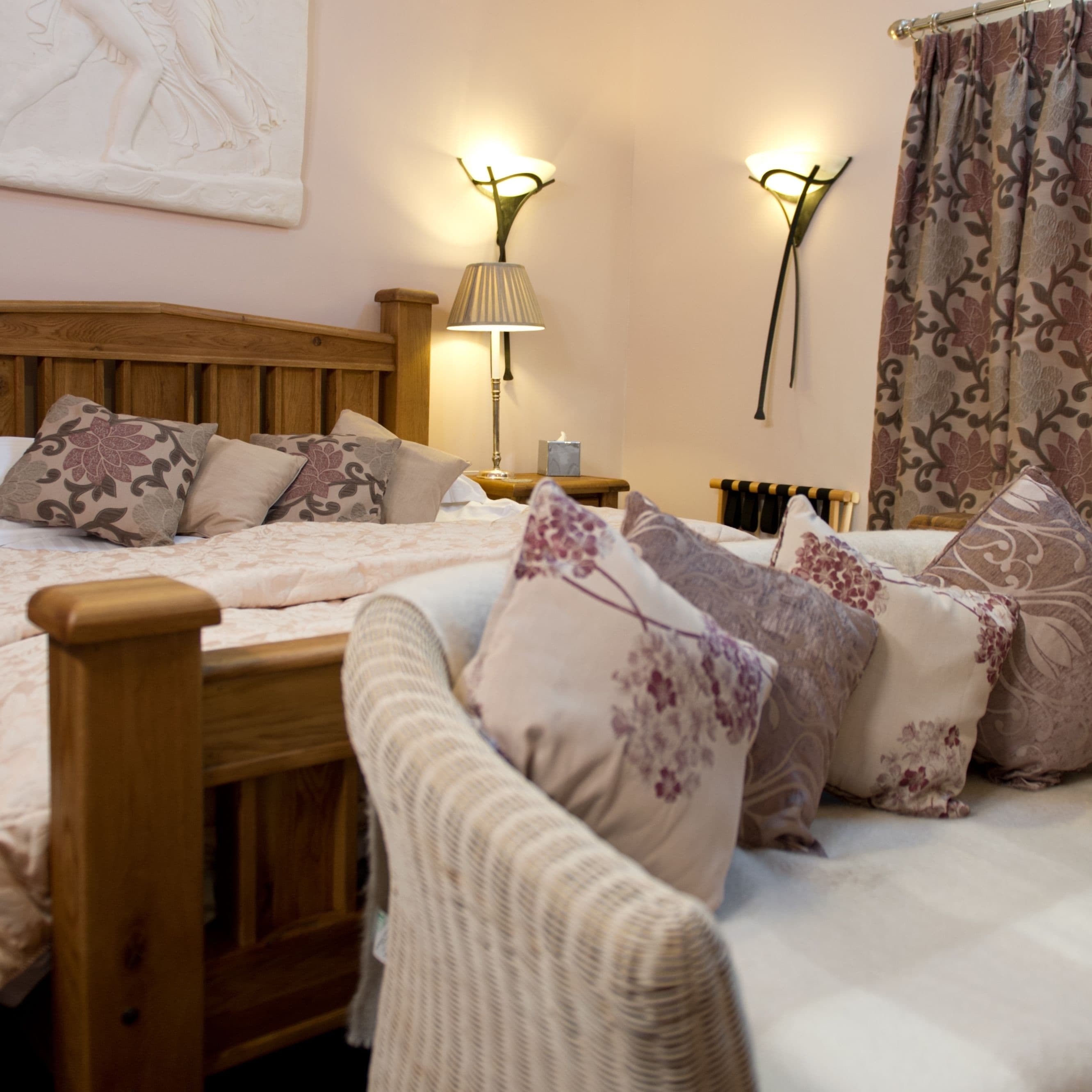 A bedroom with a wooden headboard, two bedside tables, a nightstand, a chair, and a bed with floral-patterned bedding.