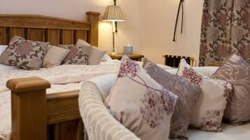 A bedroom with a wooden headboard, two bedside tables, a nightstand, a chair, and a bed with floral-patterned bedding.