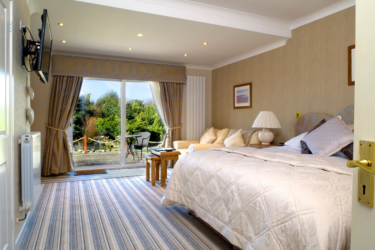 A hotel room with a large bed, a sitting area with a table and chairs, and a view of the outdoors.