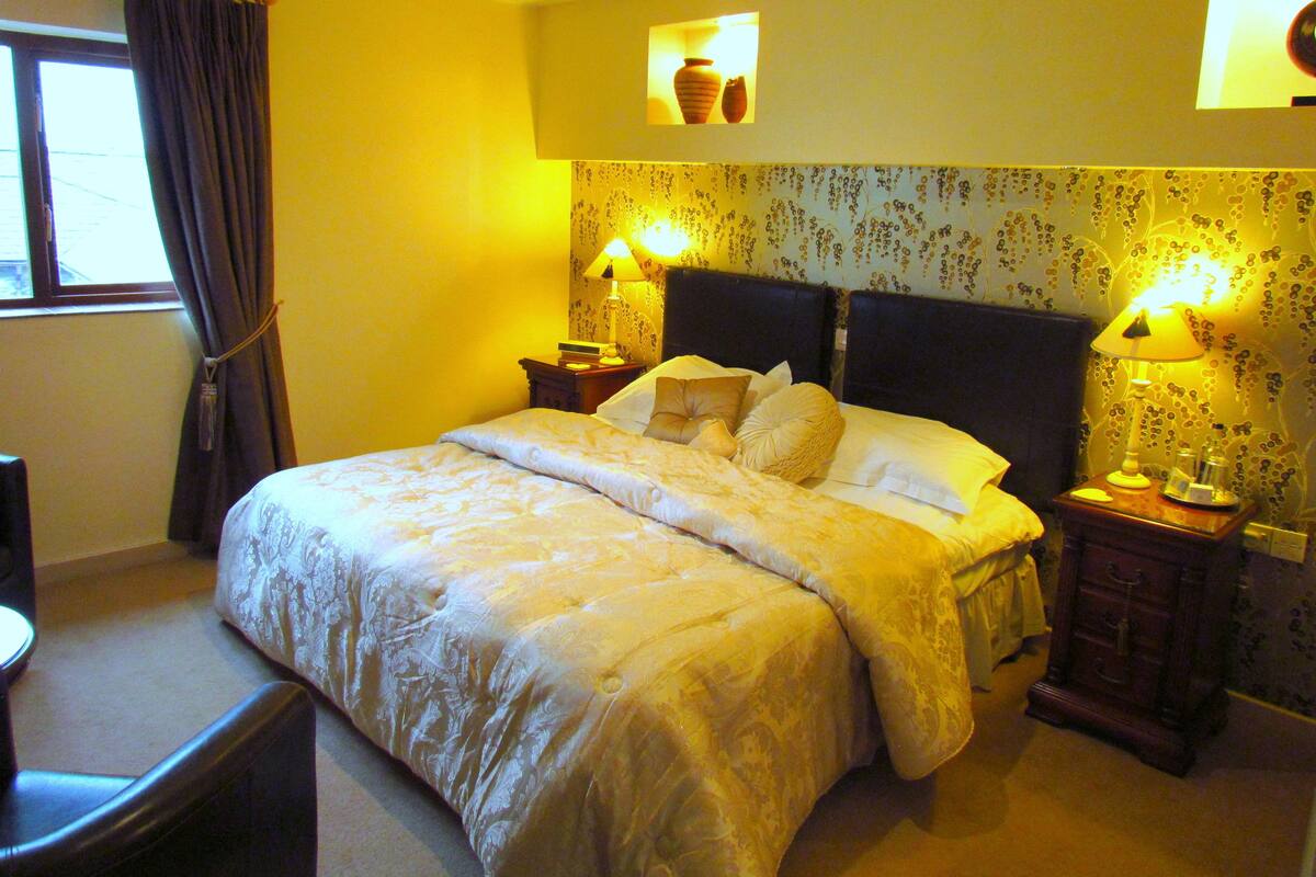 A hotel room with a large bed, two bedside tables with lamps, a chair, and a window with curtains.