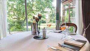 Une table ronde recouverte d’une nappe, agrémentée d’un verre à vin, d’une bouteille et d’un petit objet décoratif.