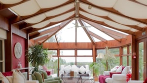 Un salon spacieux doté d’un haut plafond, de grandes fenêtres et de différents types de sièges, notamment des canapés et des fauteuils.