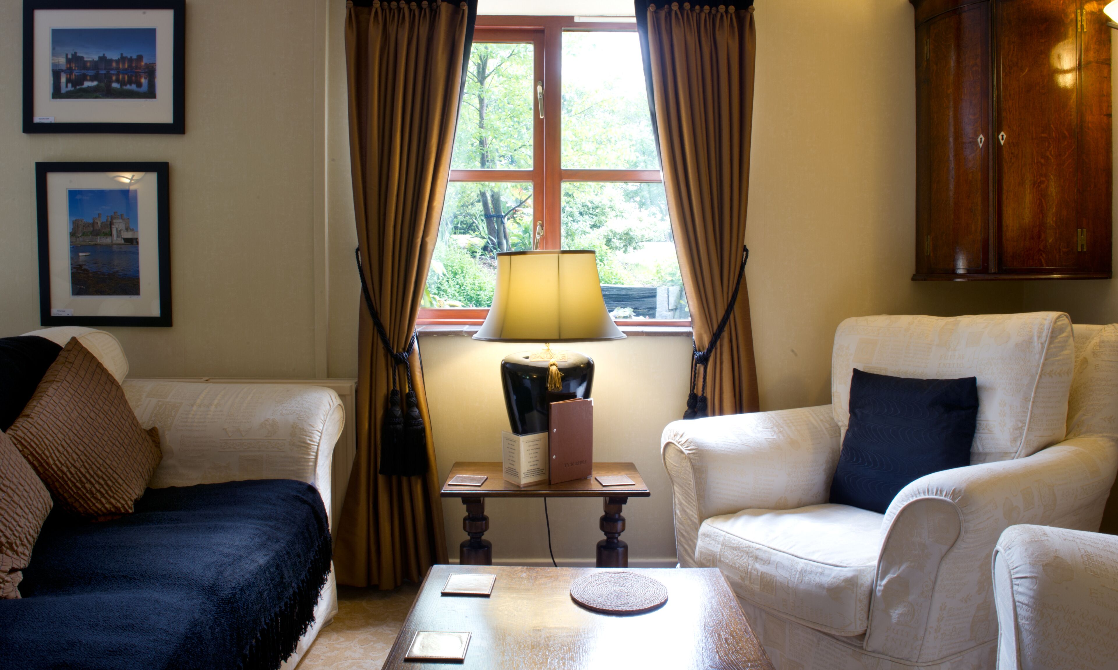 Een kamer met twee fauteuils, een tafeltje met een lamp en een raam met gordijnen.