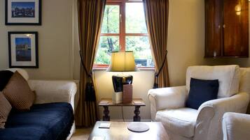Een kamer met twee fauteuils, een tafeltje met een lamp en een raam met gordijnen.