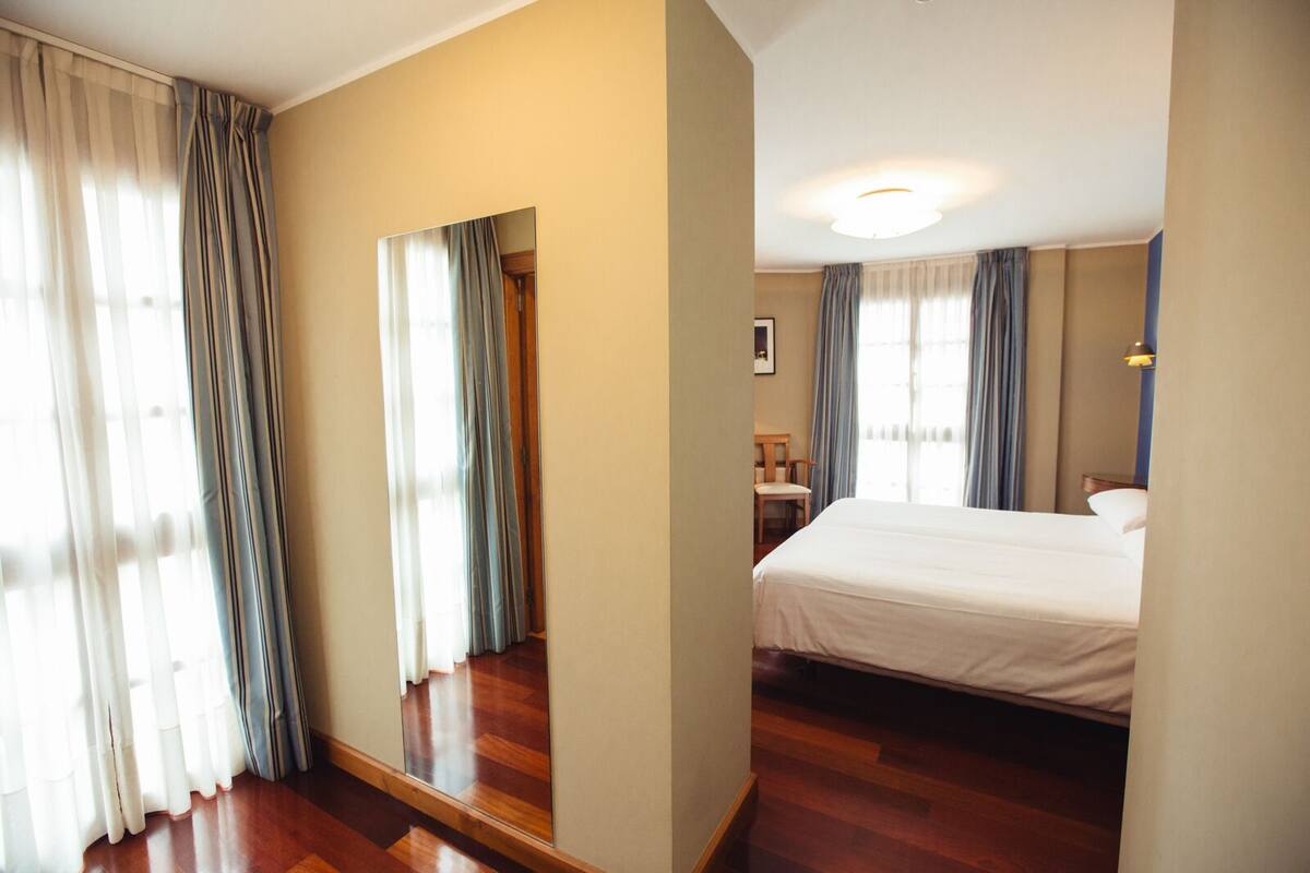 A hotel room with a large bed, wooden flooring, a mirror, and curtains.