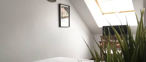 A bedroom with a skylight, a bed, a framed picture, and a potted plant.