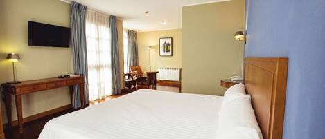A hotel room with a large bed, a desk, a chair, a lamp, and a flat-screen TV.