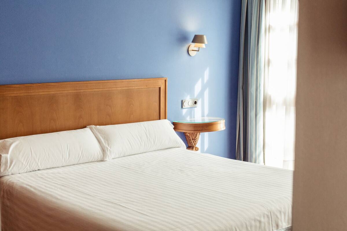 A neatly made bed with white linens, a wooden headboard, and a bedside table with a lamp.