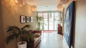 A hallway with a wooden bench, potted plants, framed pictures on the wall, and a large painting.