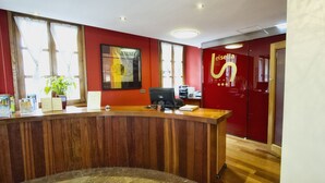 A reception desk with a wooden finish, a potted plant, and a framed artwork on the wall.