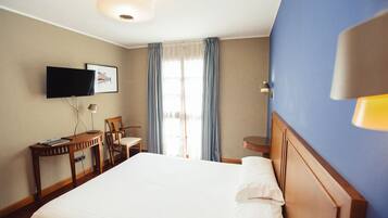 Een hotelkamer met een bed, een bureau met stoel, een televisie en een raam met gordijnen.