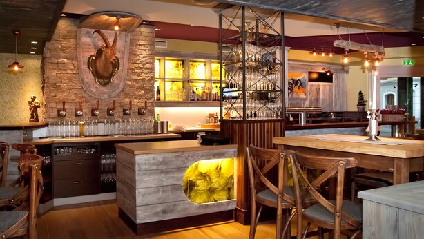 A restaurant interior with a bar area, wooden furniture, and a stone wall with a mounted animal head.