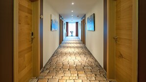A hallway with wooden doors, stone-patterned flooring, and framed artwork on the walls.