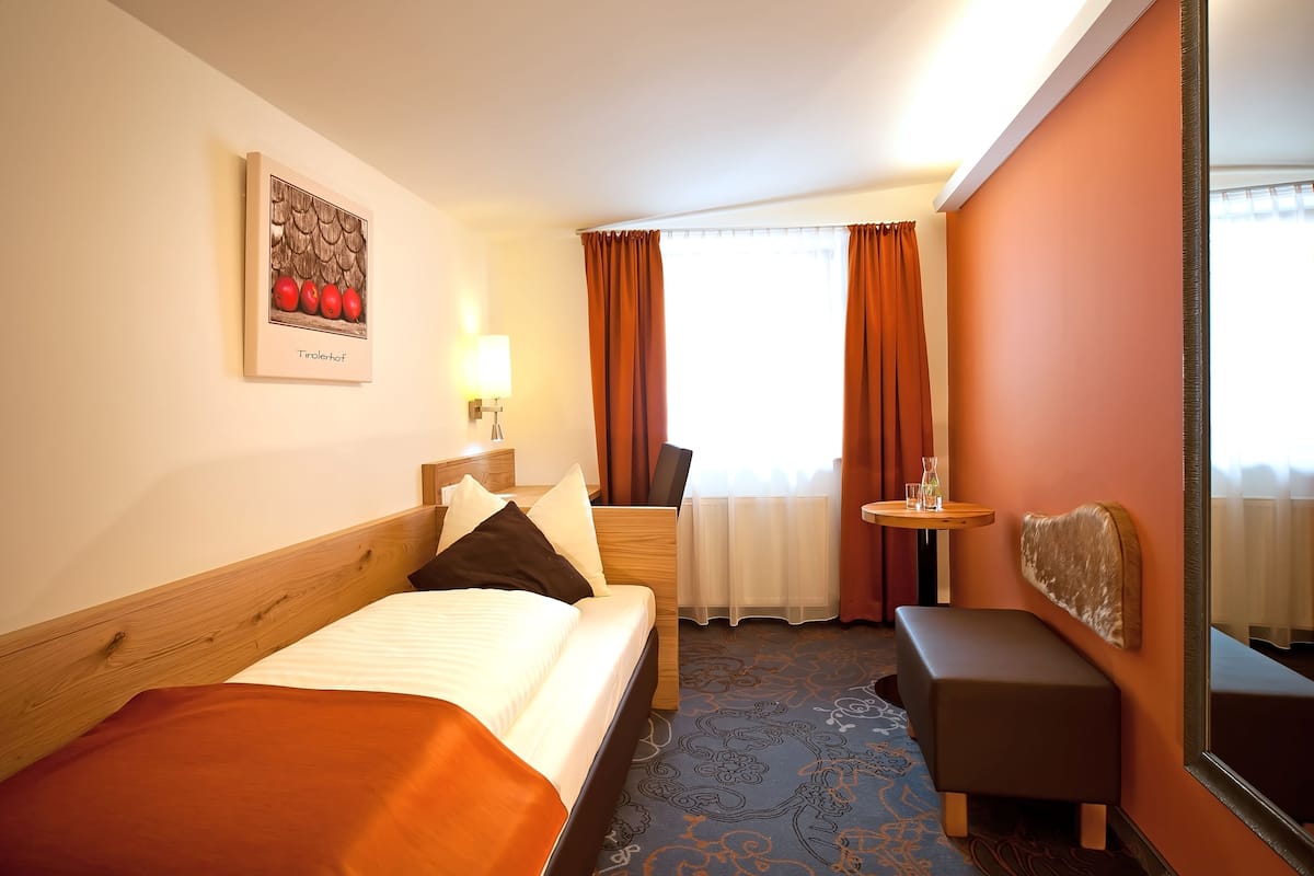 Een hotelkamer met een bed, een tafeltje, een bankje, een spiegel en een raam met gordijnen.