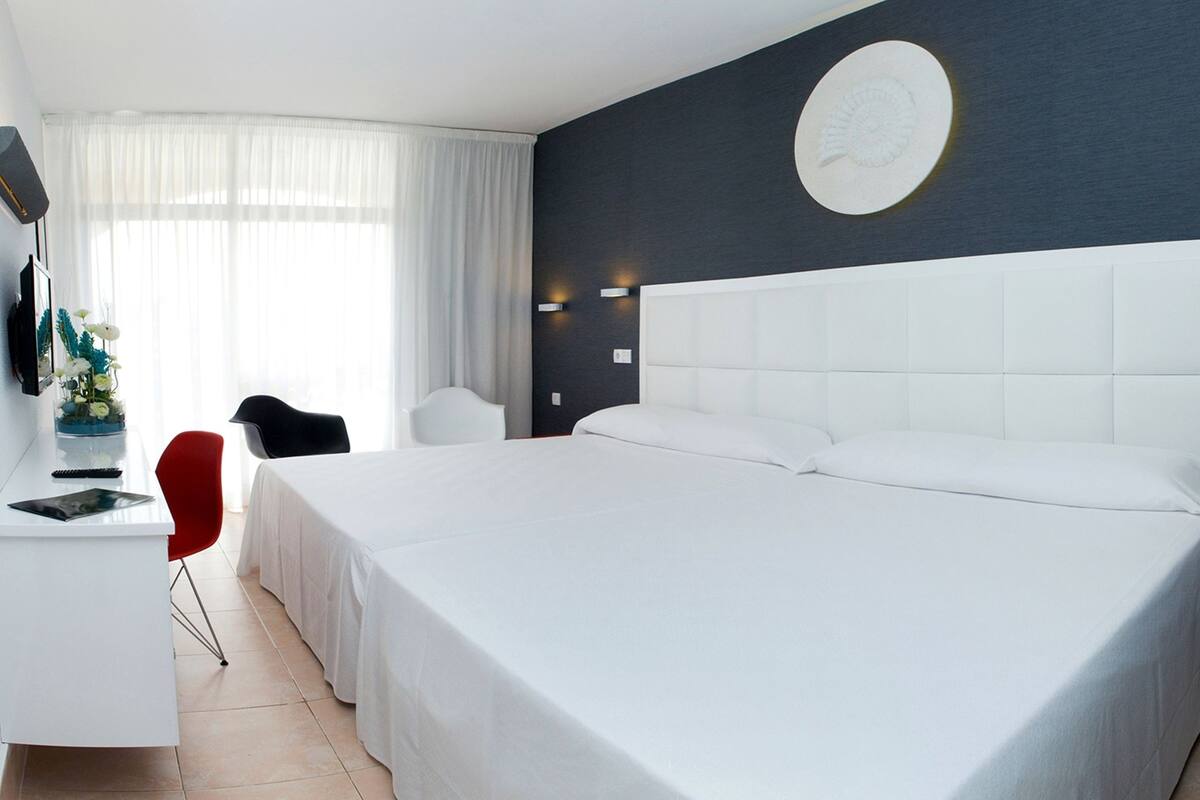 Une chambre d’hôtel moderne avec un grand lit, un bureau avec une chaise, une petite table avec un vase et un téléphone fixé au mur.