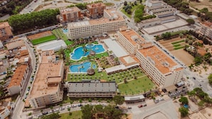 Vista aérea de un hotel con varias construcciones, una piscina central y abundante vegetación.