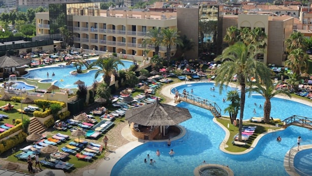 Un resort con varias piscinas, tumbonas y palmeras.