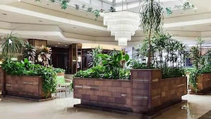 Un lobby amplio con techo alto, ventanas grandes y una exhibición de plantas en el centro.