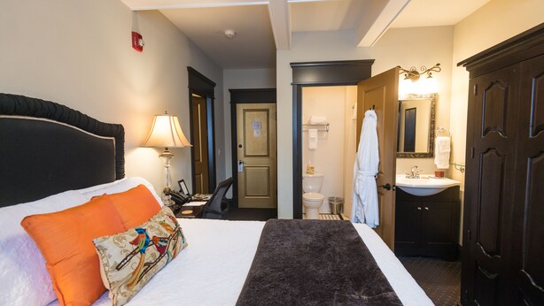 A hotel room with a bed, a desk, a chair, a bathroom with a sink and mirror, and a wardrobe. - Camas Boutique Hotel (Camas)