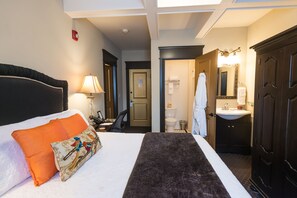 A hotel room with a bed, a desk, a chair, a bathroom with a sink and mirror, and a wardrobe. - Camas Boutique Hotel (Camas)
