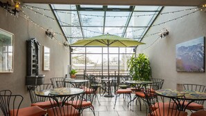 An indoor patio area with round tables and chairs, string lights, and a large green umbrella. - Camas Boutique Hotel (Camas)