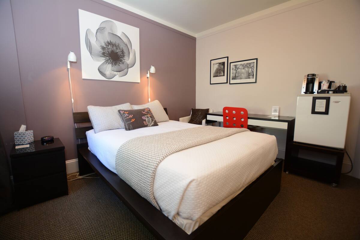 Une chambre bien rangée, avec un grand lit, des tables de chevet, un bureau et un réfrigérateur.