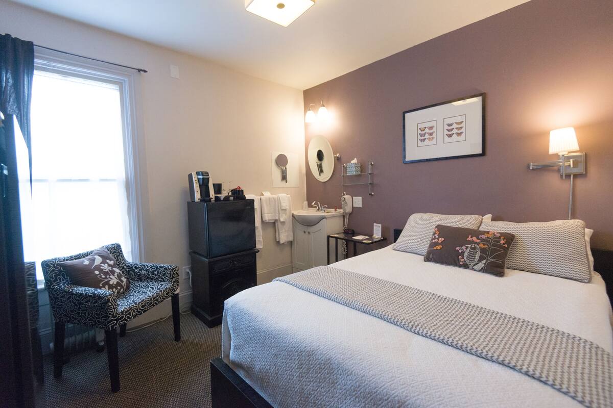 Une chambre d’hôtel avec un grand lit, une table de chevet, une chaise, un bureau, un miroir et une fenêtre.