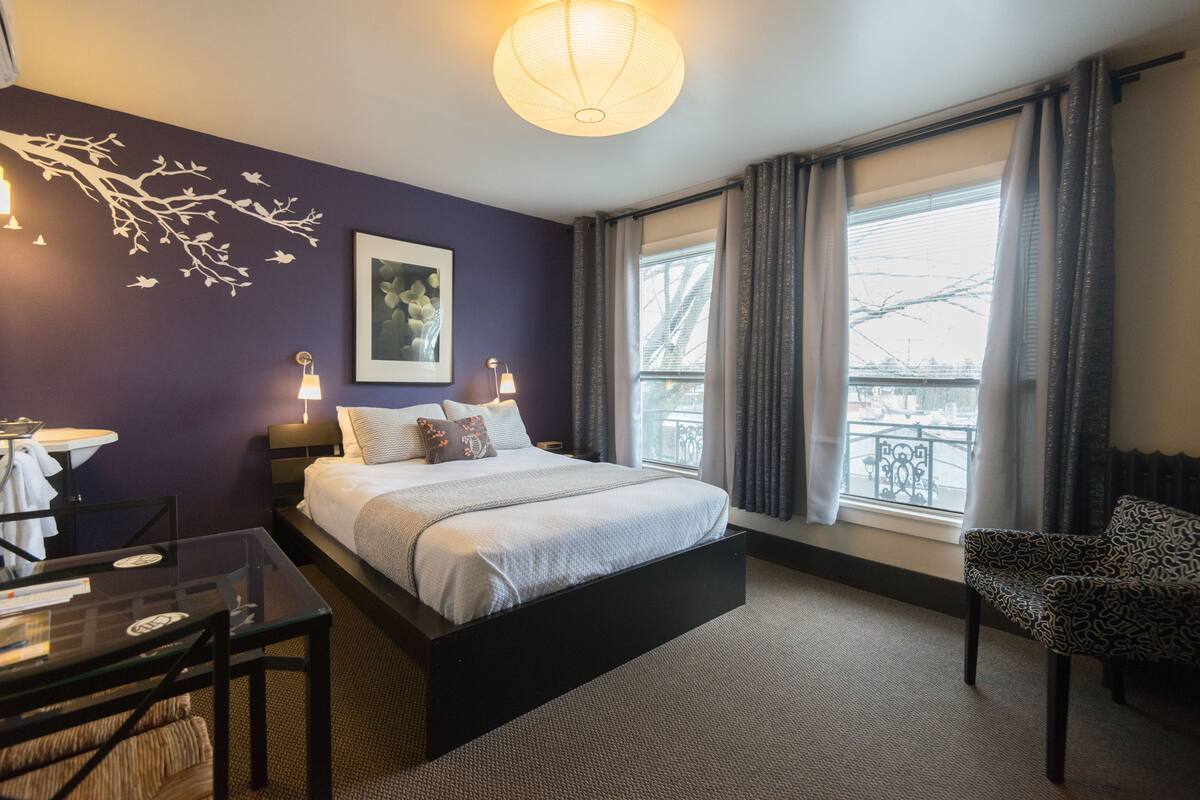 Une chambre d’hôtel moderne avec un grand lit, une table en verre, une chaise et une vue sur la ville par la fenêtre.