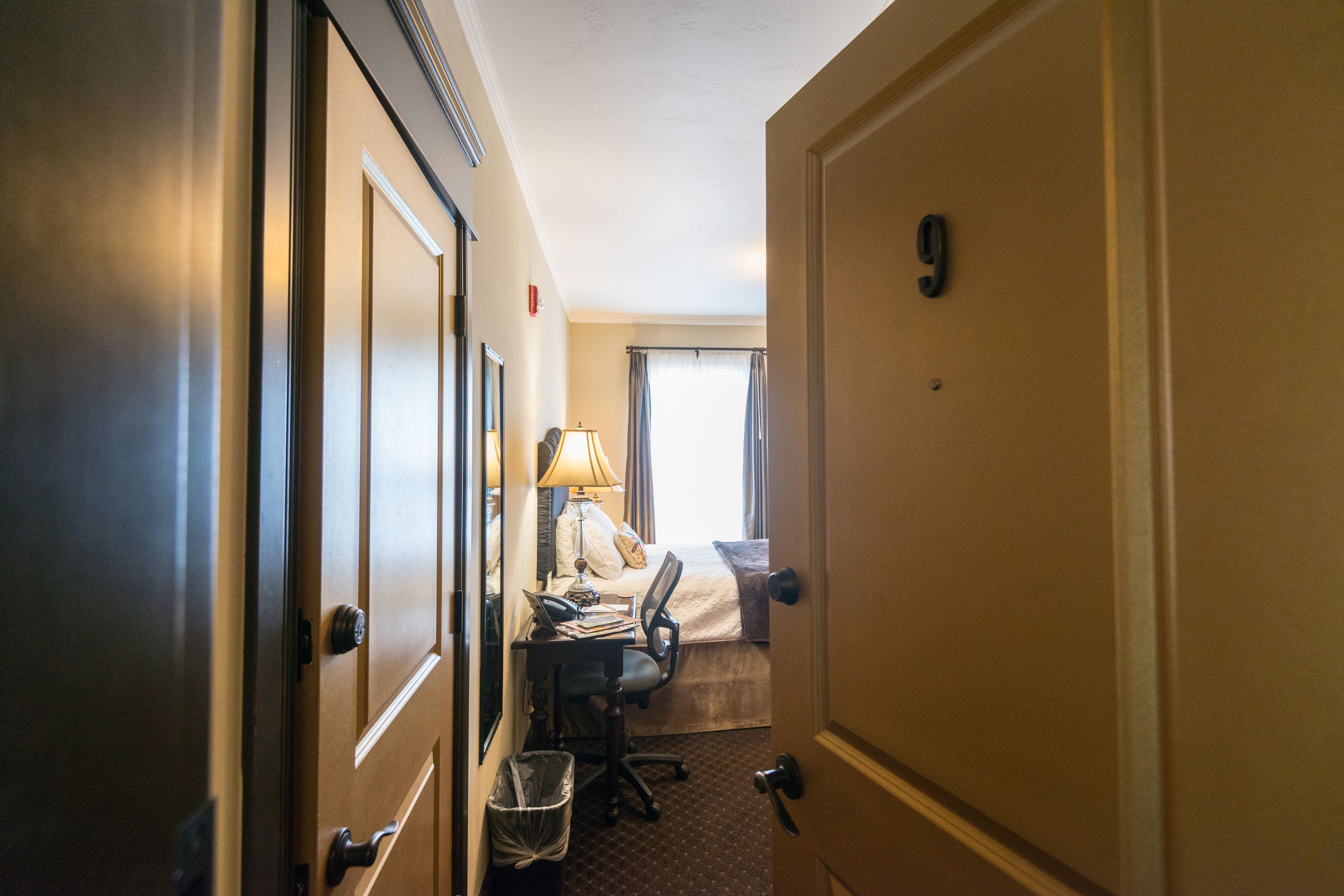 A hotel room with a bed, desk, chair, and a trash bin.