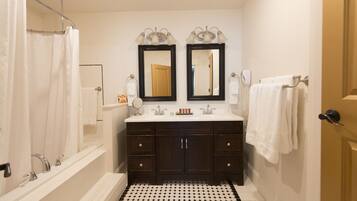 A bathroom with a bathtub, double sink vanity, two mirrors, and a black and white tiled floor.