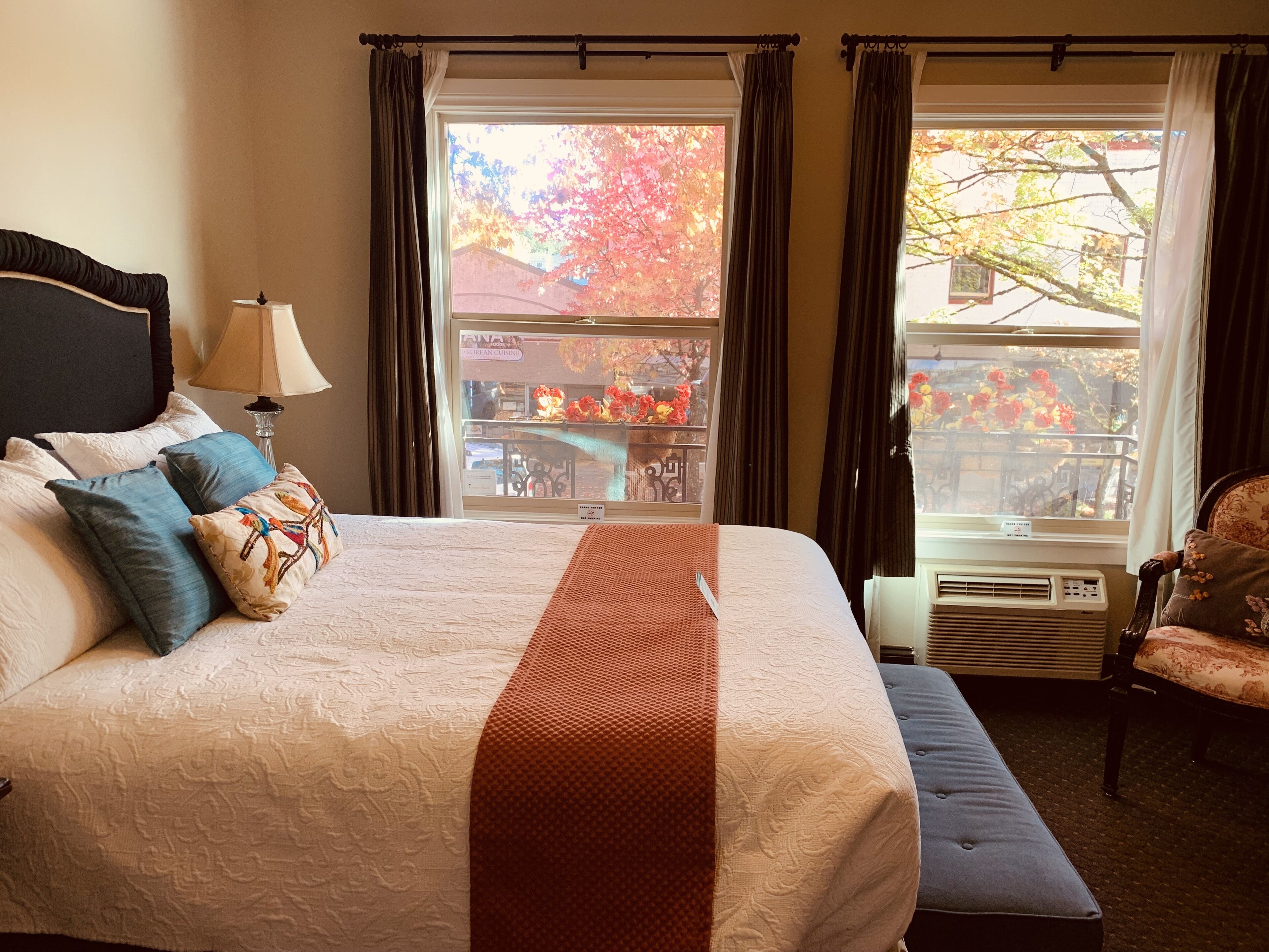 Una habitación de hotel con una cama grande, una ventana con cortinas, una silla y una lámpara.