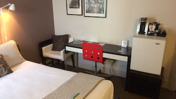 Une chambre d’hôtel comprenant un lit, un bureau, une chaise, un petit réfrigérateur et deux tableaux encadrés accrochés au mur.