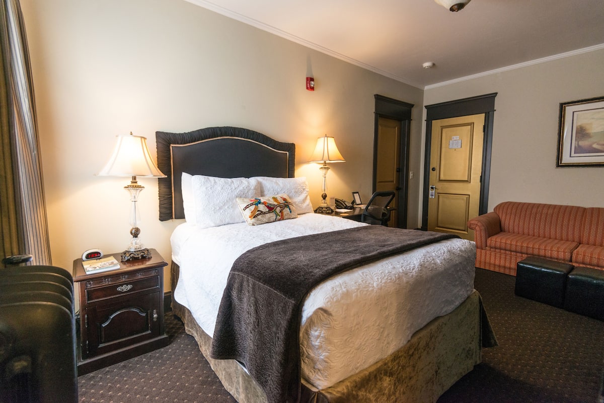 Une chambre d’hôtel avec un grand lit, deux lampes de chevet, une table de chevet, une chaise, un canapé et une porte.