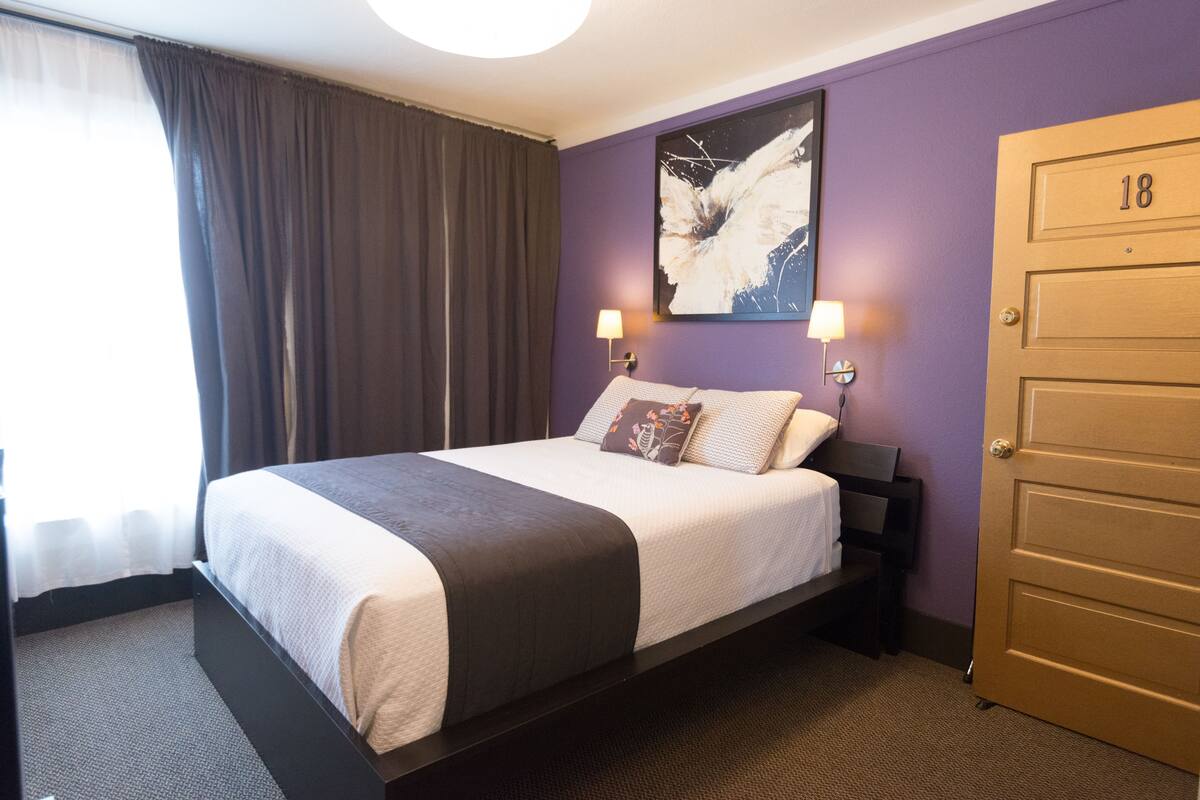 Une chambre d’hôtel avec un lit, une porte portant le numéro « 18 » et un tableau accroché au mur.