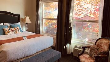 A hotel room with a large bed, a bench, a chair, and a window with autumn foliage view.