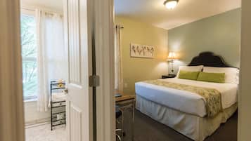 Habitación de hotel con cama, mesita de noche, lámpara, ventana con cortinas y un cuadro de un pájaro en la pared.