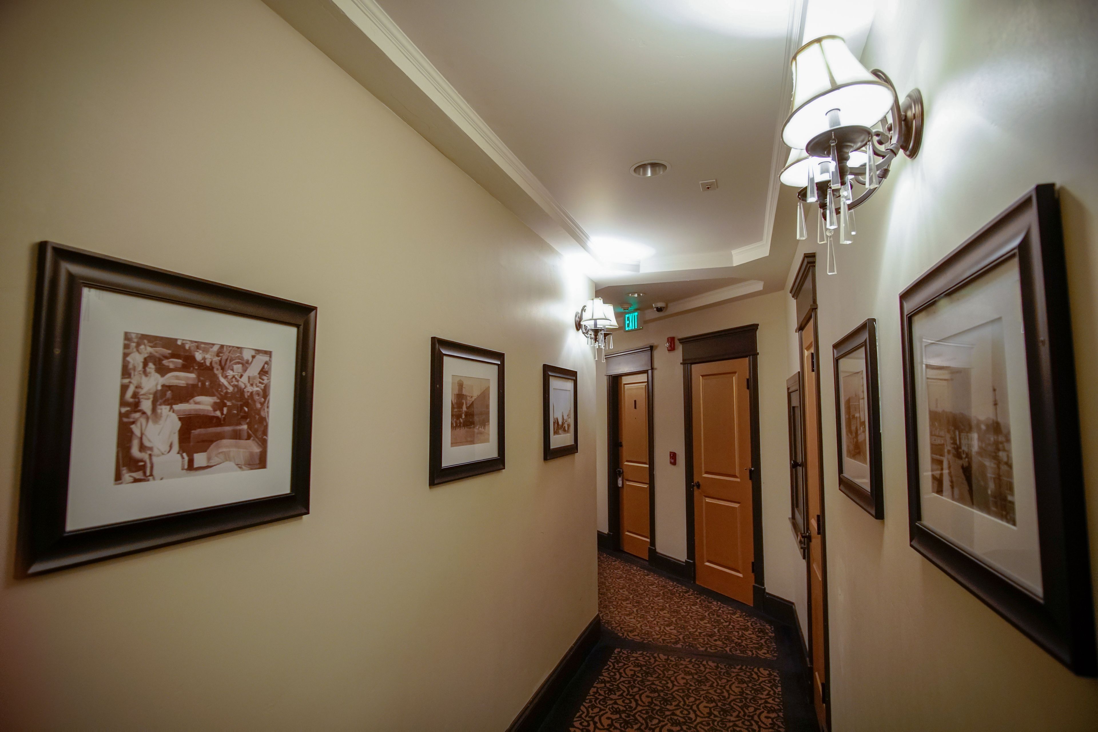 A hallway with framed pictures on the walls, a patterned carpet, and a chandelier.