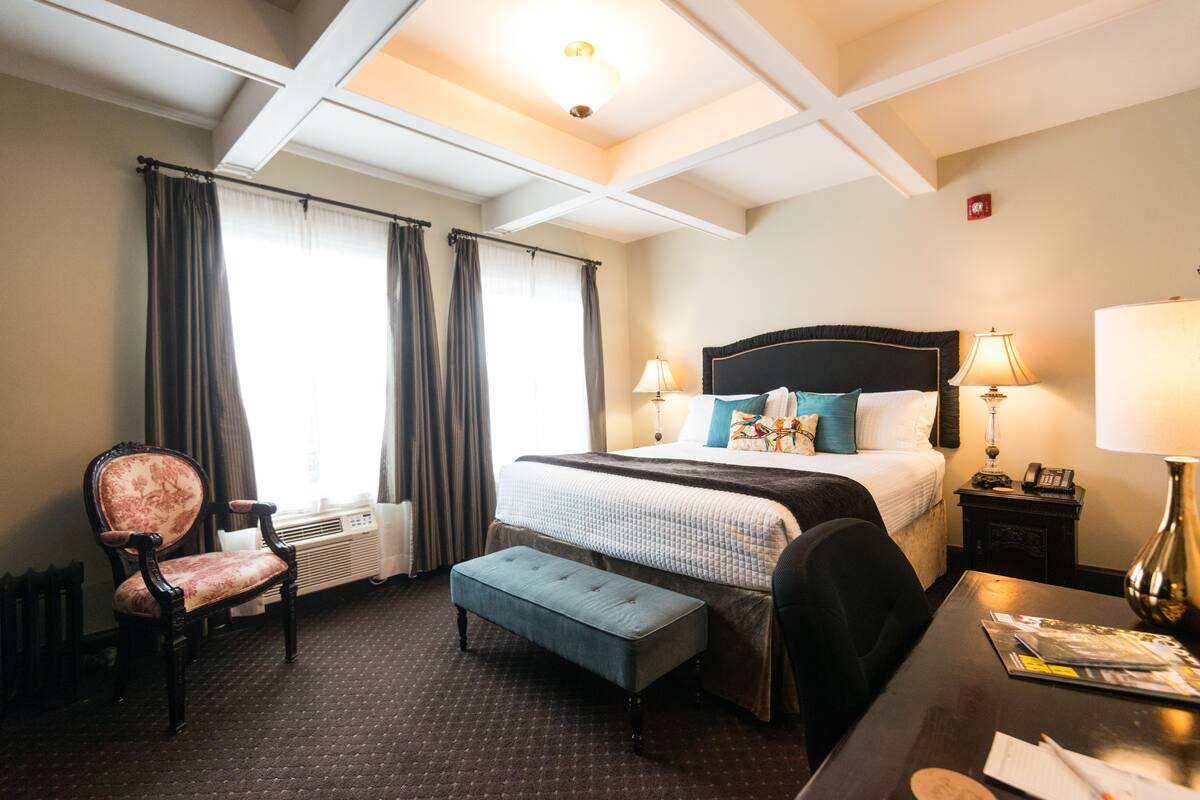 Une chambre d’hôtel avec un grand lit, un bureau avec une lampe, une chaise et une fenêtre avec des rideaux.