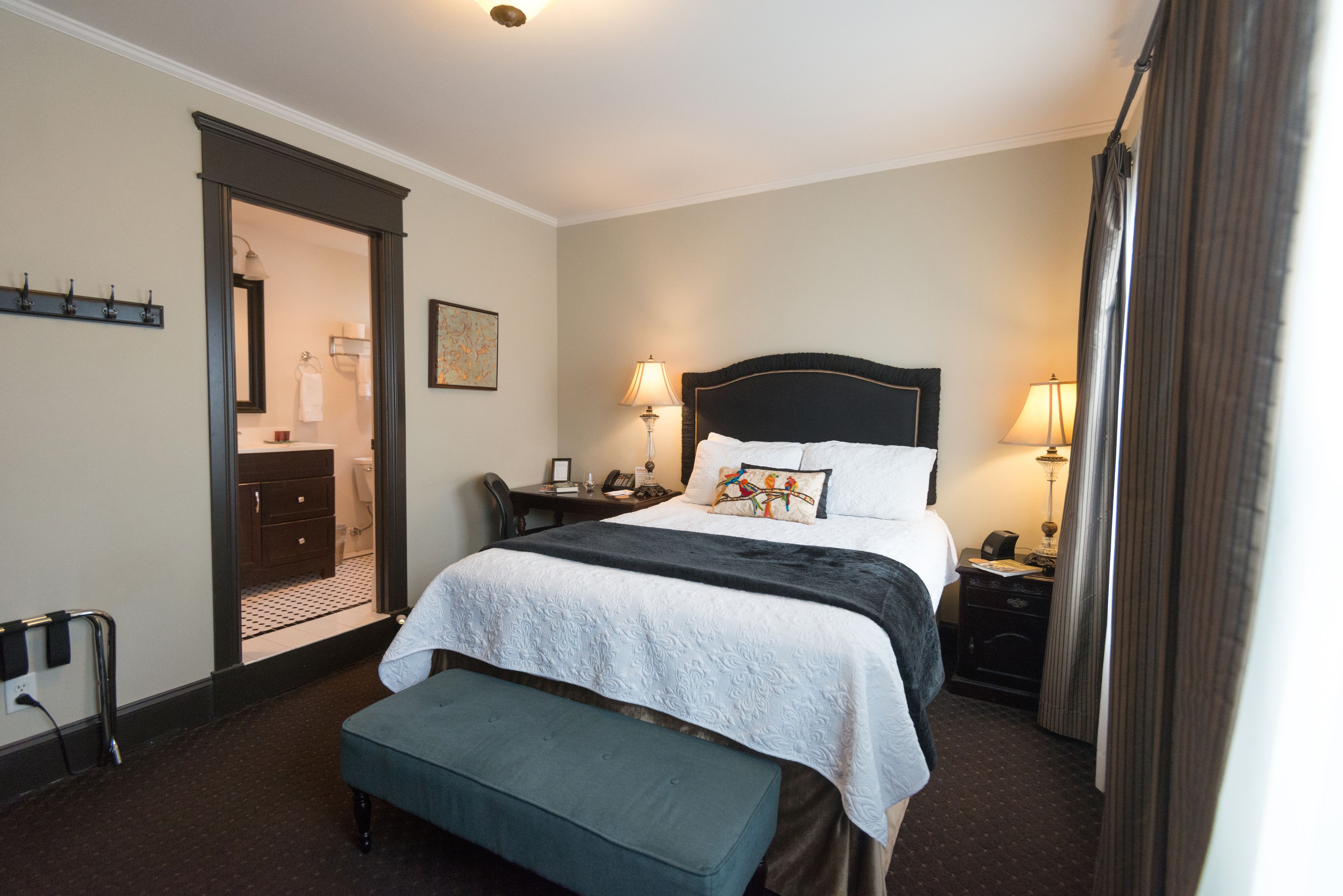 A hotel room with a large bed, bedside tables, a bench, a desk, and a bathroom visible through an open door.
