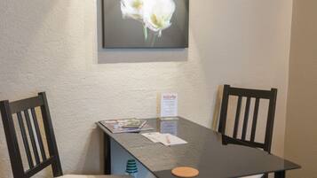 A hotel room with a dark wooden table, two chairs, a framed floral artwork on the wall, and a small welcome sign.